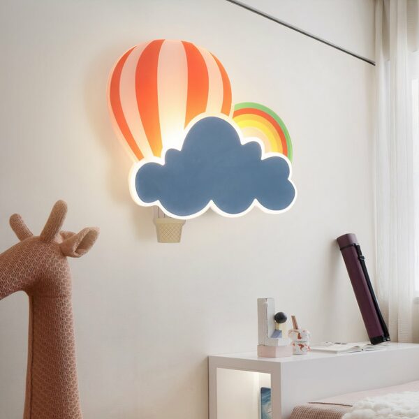 On the wall of a children's bedroom, in the center of the picture, you'll see a cloud, hot-air balloon and rainbow-shaped wall sconce for a children's bedroom. At the bottom left of the picture, there's a pink giraffe toy head.