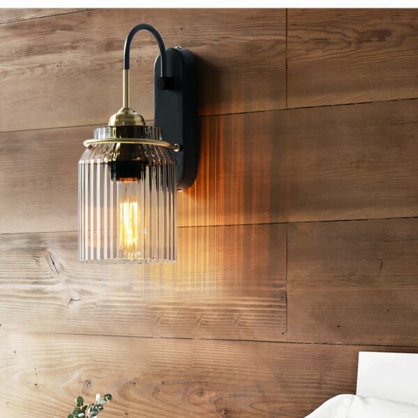 Industrial-style glass wall light with black metal bracket against a wooden wall