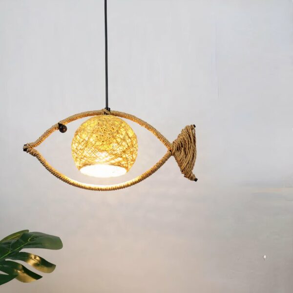 Suspended chandelier made of rope wrapped around a fish-shaped metal rod. With a ball-shaped lampshade in the center. Behind is a gray wall, and below left is a piece of green plant.