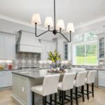 Industrial-style black wrought-iron chandelier. Composed of a central vertical bar linking a round base that hangs from the ceiling, to a ball from which a shaft descends and rises on either side to accommodate white fabric shades. On a white background.