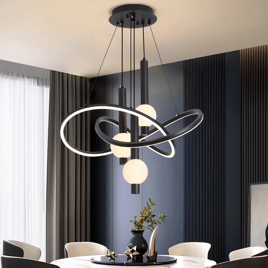 Black chandelier with black support fixed to the ceiling, from which cables descend to hold intertwined rounded structures that are luminous and black on the outside. In the center of these structures hang black tubes with a lighted ball. Fixed above a round white marble-style table with round black top, a vase on top and decorative objects. 6 armchairs around the table, to the left a bay window with a grey curtain and the wall opposite is duck-blue with vertical grooves.