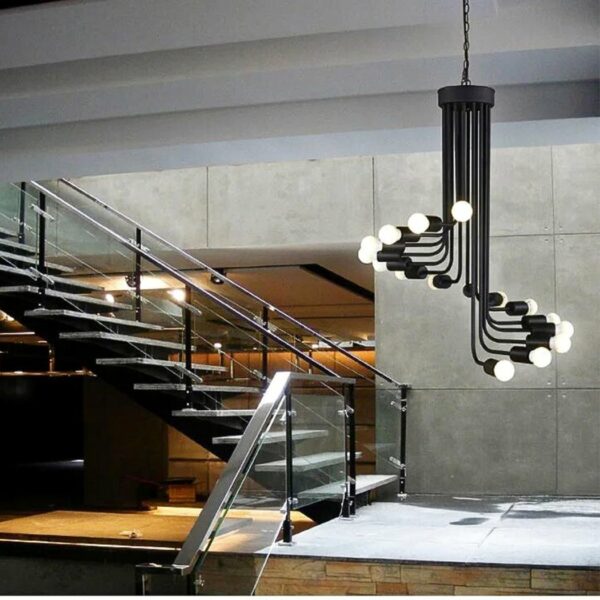 a black wrought-iron chandelier with exposed bulbs can be seen in a living room with stairs in the background