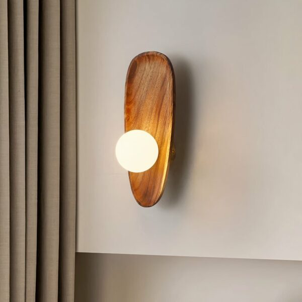 Wooden wall sconce in the shell style with large pearl light, hung on a white wall next to a taupe-colored curtain.