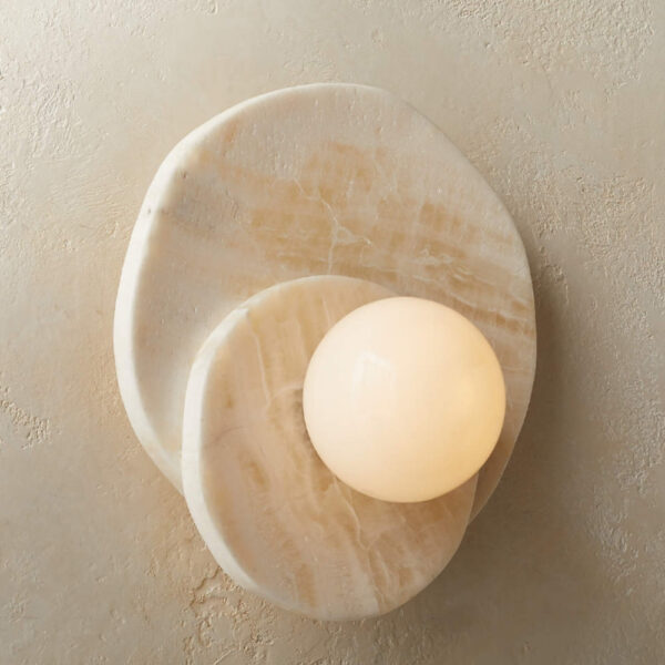 Circular wall light natural stone in beige colour with two stone circles one on top of the other. In the centre, a luminous sphere. The wall light is fixed on a beige wall.