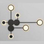 Black geometric wall light with six circles glowing warm against a grey wall