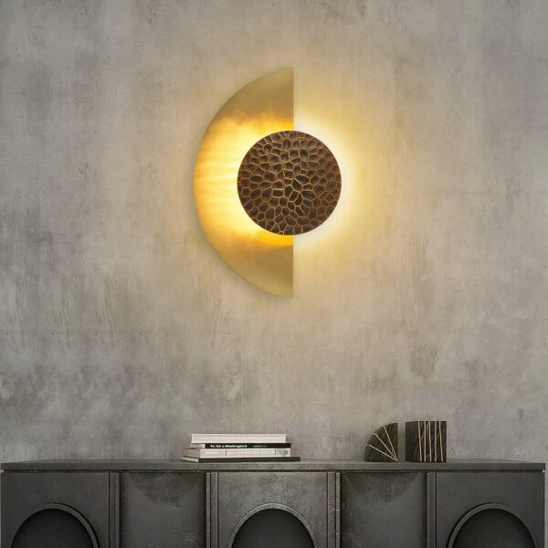 On a dark gray wall, a wall sconce hangs in the center in the shape of a lit golden half-moon.