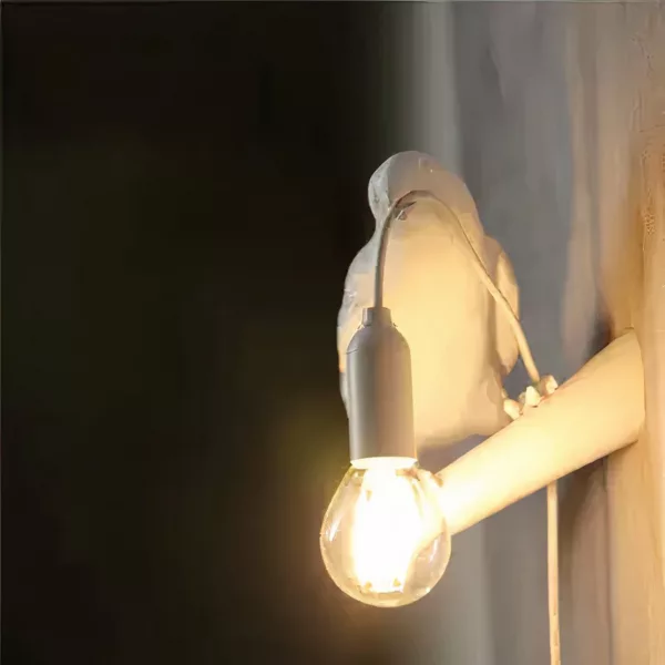 On a black background, a white raven-shaped wall light is lit.