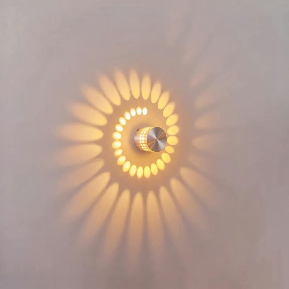 Circular LED wall light in aluminium with light projection Round LED wall light in silver aluminium, switched on, casting a spiral of warm light on a white wall