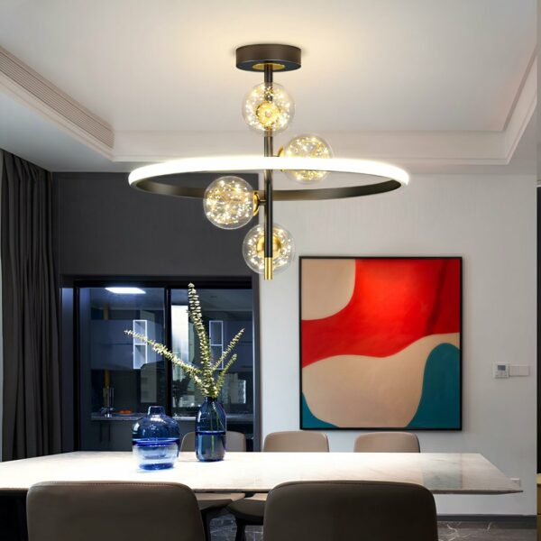 Chandelier with round black ceiling support, a black vertical fixture attached to it. 4 transparent balls with gold wires inside and light diodes giving the impression of twinkling. The whole is surrounded by a luminous circle on the outside and black on the inside. Fixed above a white rectangular table with 5 grey chairs around it. 2 blue vases on the table filled with water, one with long flowers. On the opposite wall, a beige, red and blue abstract frame. To the left, a bay window with gray wall, black frame and gray curtain.