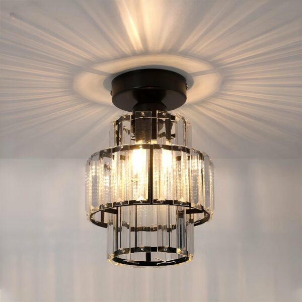 Cylindrical ceiling chandelier with 3 rows of crystal-style slats. The ceiling support is black and the slats are mounted on black circles. The bulbs are lit and emit rays to the ceiling around the chandelier.