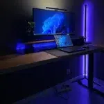 Purple LED corner floor lamp glowing beside a desk with monitor and laptop
