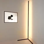 Black corner floor lamp with warm white light beside an abstract framed artwork