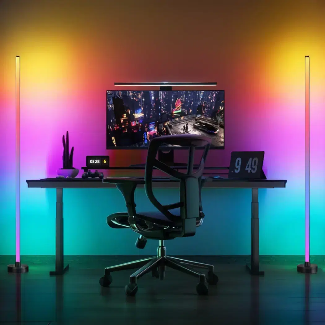 Two rainbow LED floor lamps flanking a gaming desk with colorful wall glow