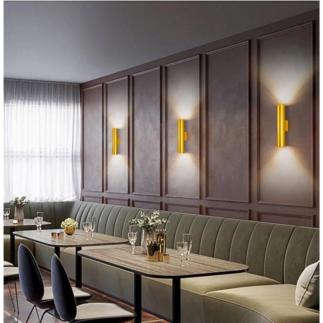 Three gold vertical bar wall lights glowing up and down on a panelled dining room wall