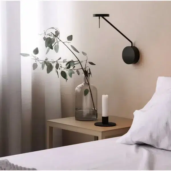 Black swing-arm wall light with a slim angled arm beside a bed