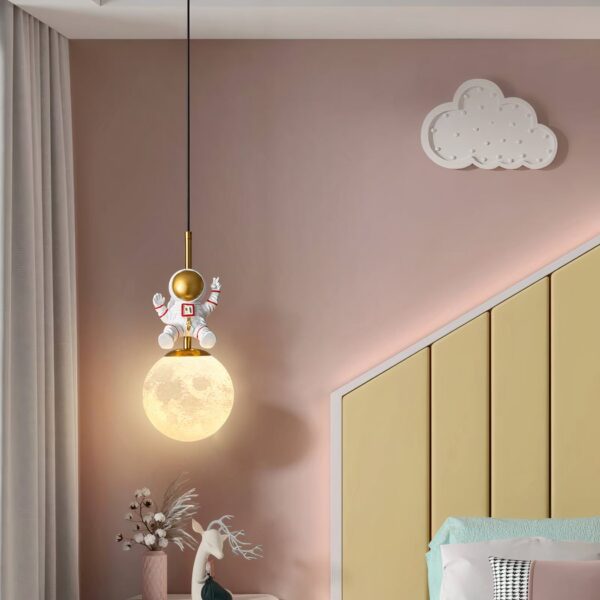 Gold pendant light with an astronaut figure sitting on a glowing moon shade
