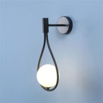 Black wall light with a teardrop shaped loop holding an opal glass ball