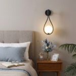 Teardrop shaped wall lamp above a wooden nightstand beside the bed