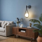 Black wall light with a looped cord and a round glass globe above a wooden sideboard