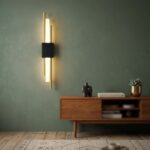 Vertical gold linear wall light with a black bracket above a wooden sideboard