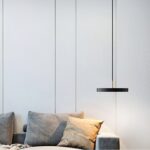 Black disc pendant with a brass stem hanging low beside a grey sofa with cushions