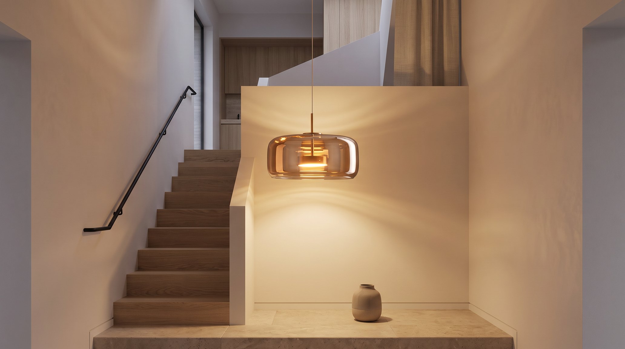 Stairwell in the evening with a round cognac smoked glass and copper LED pendant light glowing warm white beside an oak staircase with a black handrail, above a pale stone landing